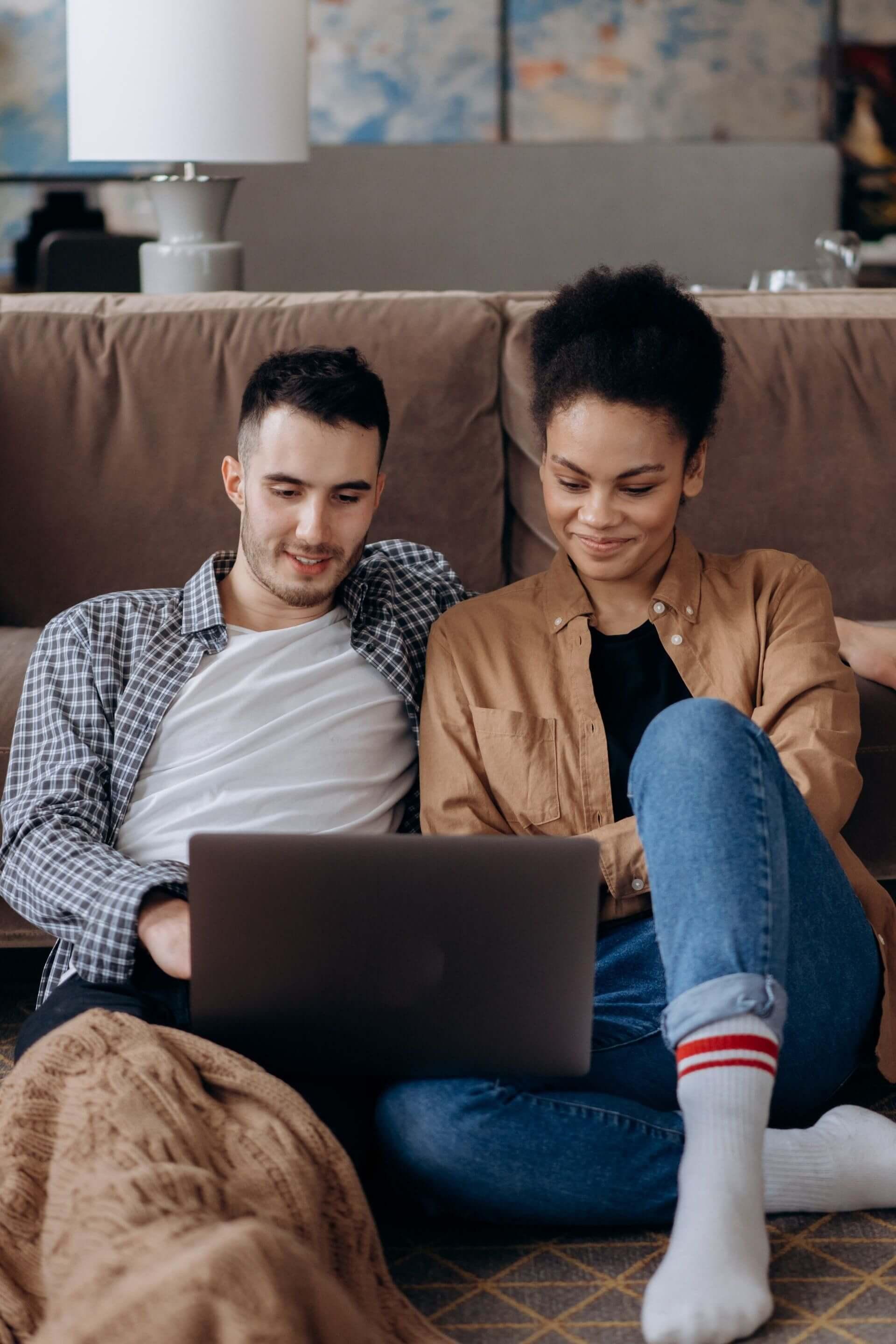 Man and woman sitting on couch holding a laptop.