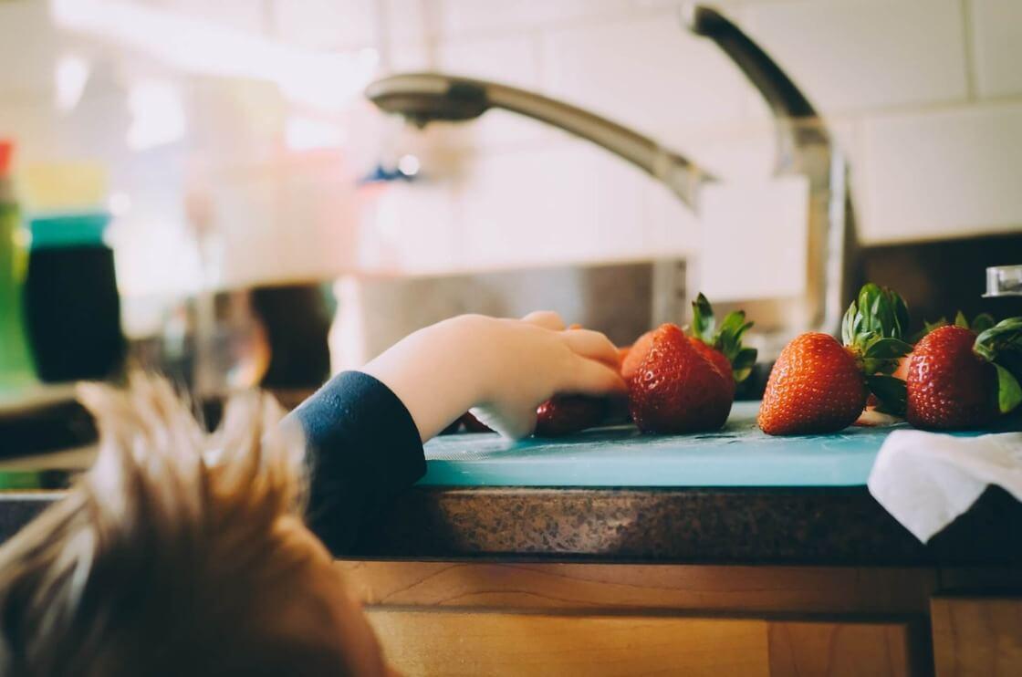 Young boy reaching for strawberry on countertop.