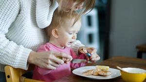 Mom teaching infant to eat with silverware.