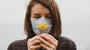 Woman smelling a flower through a mask.