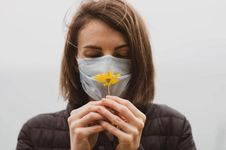 Woman smelling a flower through a mask.