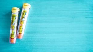 Two EpiPens lying on a blue background.