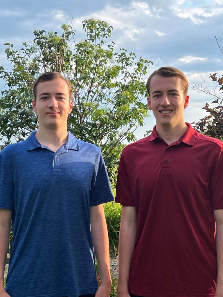 Two identical twins smiling outside.