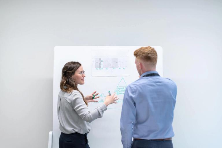 Two people brainstorming in front of a whiteboard.