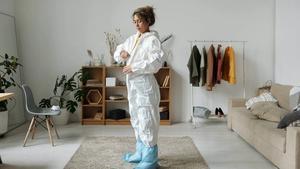 Woman zipping up hazmat suit in house.