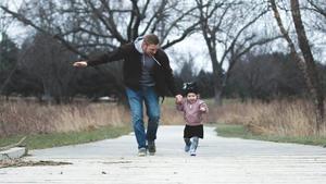 Smiling father and young daughter holding hands outside.