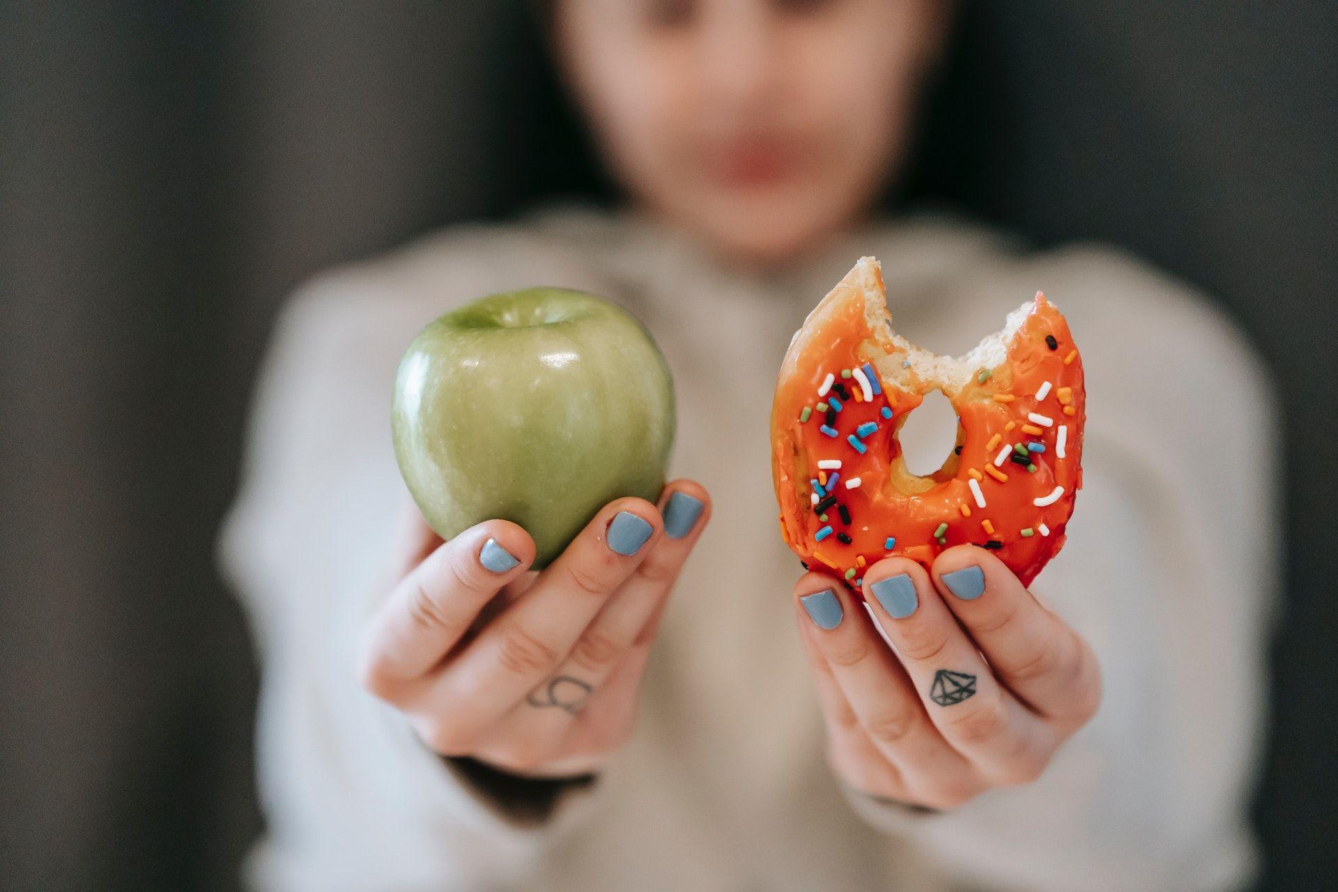 Woman holding an apple in one hand and a donut in the other.