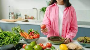 Woman holding a tomato above a counter full of vegetables.