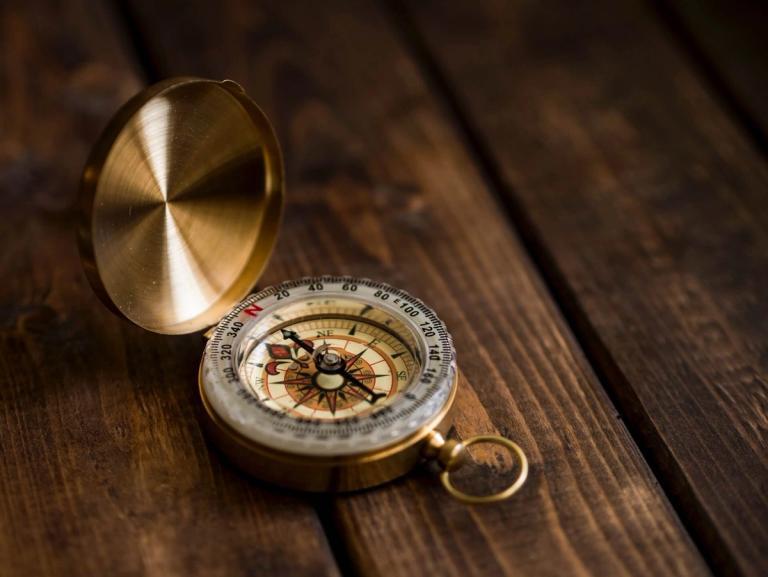 A golden compass on a wood table.