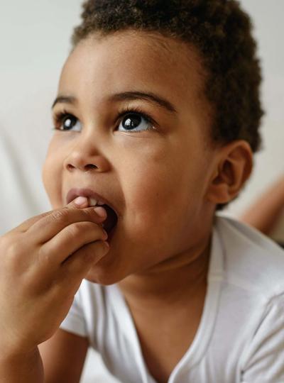 Toddler using hand to hold food in mouth.