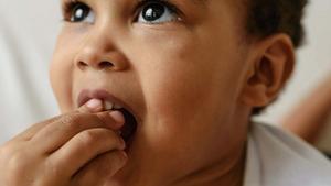 Toddler using hand to hold food in mouth.